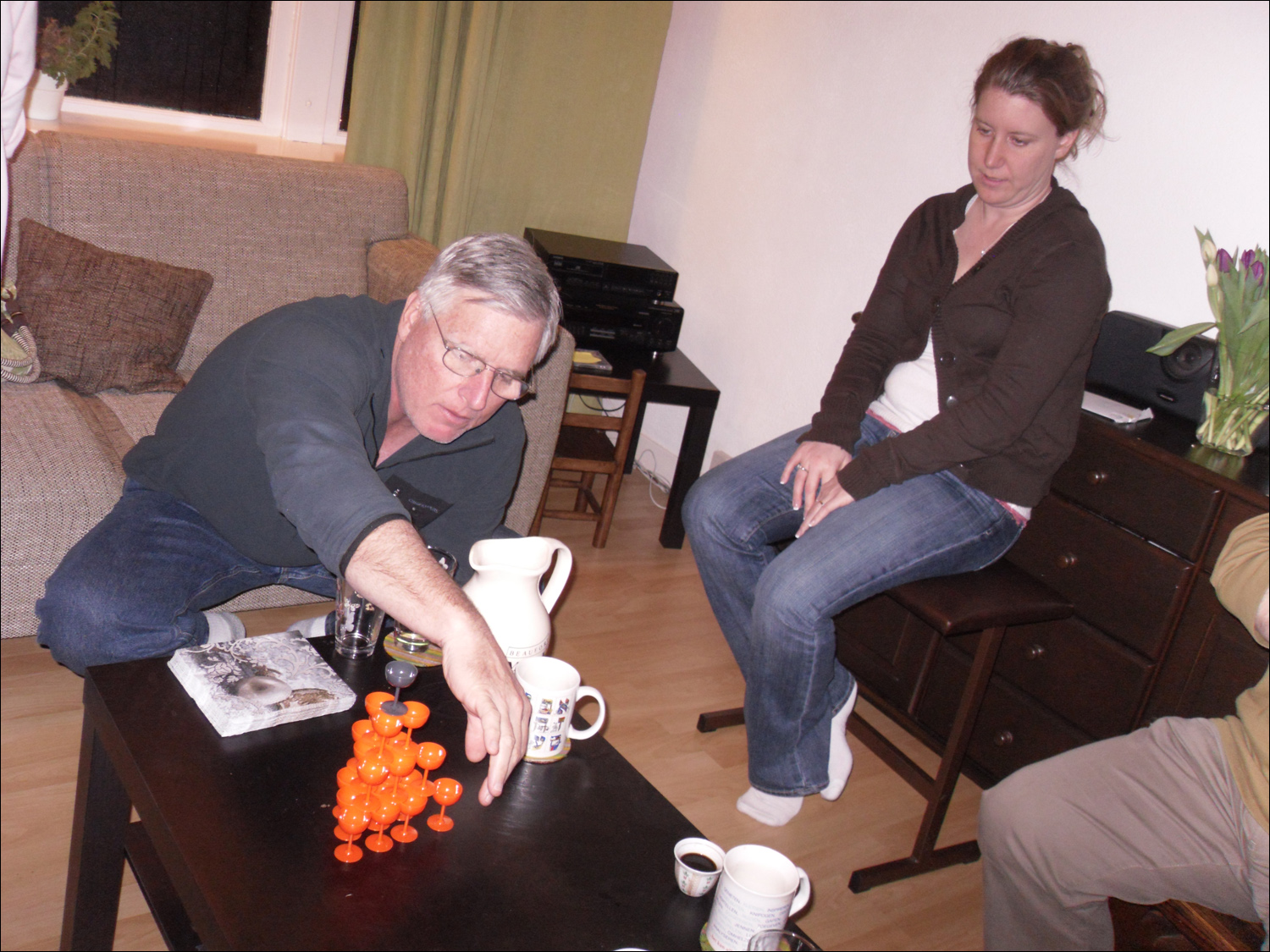 Dutch dinner and game night at home of Martijn and Joseba- Bob playing a Dutch form of Jenga with plastic glasses while Becky watches